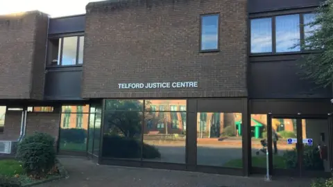 A brick building with automatic doors on the right. The front of the building has mirrored windows along the ground floor and a white sign above reads Telford Justice Centre in white writing. 
