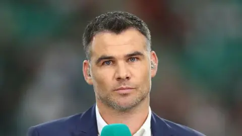 Getty Images Mike Phillips facing audience at Rugby World Cup 2019. Wearing white shirt, blue blazer, looking serious