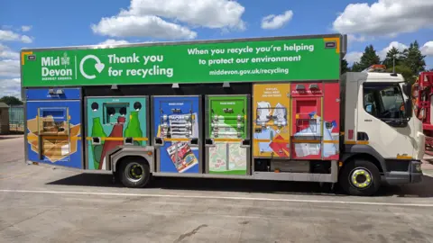 MDDC / LDRS A Mid Devon District Council recycling lorry parked in a parking area. Blue and cloudy skies.