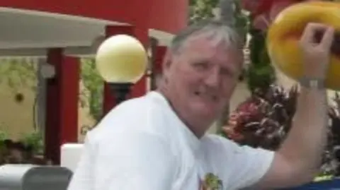 Harry Turner wearing a white top. He has grey hair. 