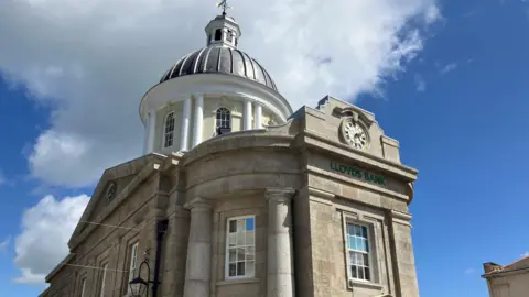 BBC The exterior of the building under a blue sky with a cloud. The dome is visible at the top