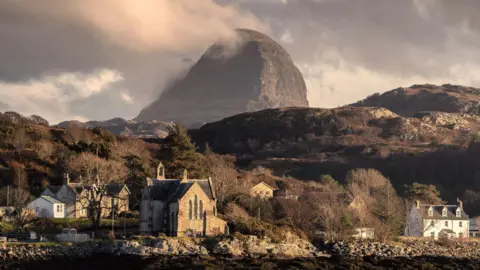 Houses and a church in Lochinver with the mountain Suilven, in the background, on a bright winter day.