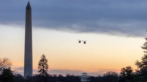 EPA The Washington Monument, a tall narrow pointed landmark against a dusklight sky, with two military helicopters in silhouette 