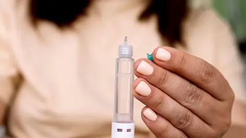 Getty Images A woman in a peach top and with peach-coloured nail polish holds a weight loss drug syringe