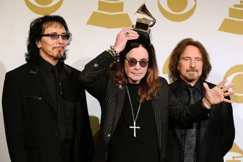 Getty Images Three members of Black Sabbath face the cameras at the Grammy Awards. In the centre, Ozzy Osbourne holds a grammy award on his head.