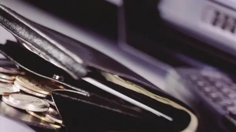 BBC A purse with coins inside and a phone on the right.