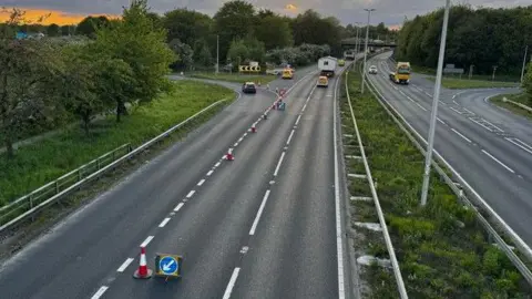 A picture of the A63. There are three lanes to the left of the picture, with a row of traffic cones along the first lane. There is a central reservation and lanes heading in the opposite direction on the other side of it.