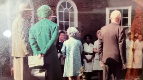 Barbara Joseph/Supplied An old photograph depicting a row of nurses in uniform in front of a red-brick building, meeting a group of men and women dressed in smartly in suits and dresses
