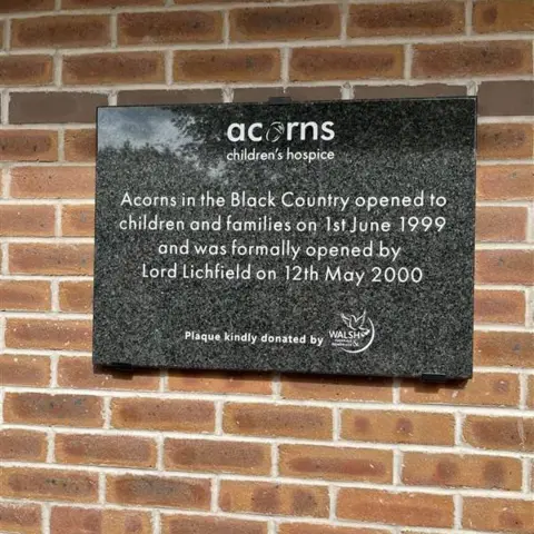 A black plaque on a brick wall, which commemorates the opening of Acorns' Walsall hospice.