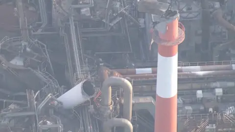 An orange chimney is seen with a broken top, surrounded by debris and rubble.