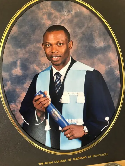 Karima Ngaage A graduation photo of Ngaage, who has short black hair. He is wearing a black gown, with a pale blue sash with white tassels. Beneath the gown he is wearing a white shirt and blue striped tie. He is holding a navy blue scroll. 
