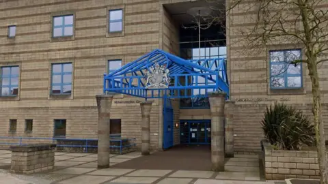 The entrance to Wolverhampton Crown Court, a brick-built building with a blue canopy resting on four pillars in front of a set of glass doors.