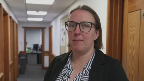 Det Insp Eleanor Atkinson wearing a black and white striped shirt and a black jacket and glasses.