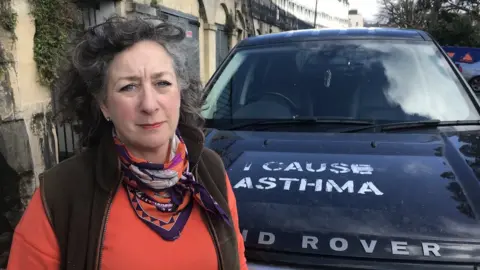 BBC A woman standing in front of a Land Rover which has been vandalised