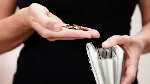 Mid section of person in black top holding purse in one hand and coins in the other.