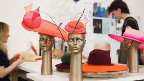 PA Media Two creative arts student in a workshop creating and drawing hats, surrounded by orange and pink hats on mannequins