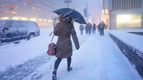 A person walks into the snow with an umbrella and their back to the camera on a snowy street in the United States.