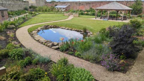 The restored garden with a pond in the foreground then a pagoda footpaths and lots of flowers 