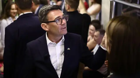 Andy Burnham reacts as he stands in a metro carriage among passengers during the journey between the metro stations Zoloti Vorota and Lukanivska on August 24, 2026 in Kyiv, Ukraine.