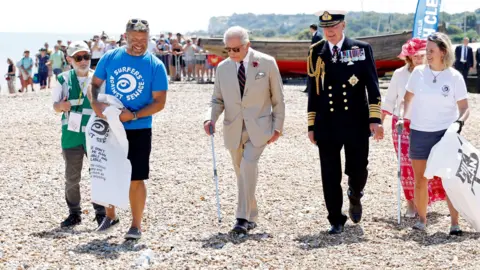 PA Media King Charles III wearing dark glasses and walking with a litter pick up stick joins a community beach clean-up initiative in Deal on the shingle beach