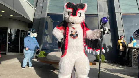 A furry dressed as a large white mythical creature, holding a magical staff.