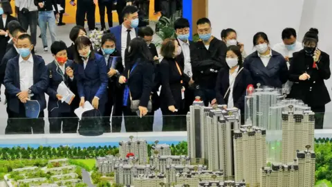 Getty Images People look at models of houses at the 2021 Dalian autumn real estate fair at Dalian World Expo Centre.