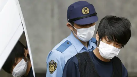 Tetsuya Yamagami, suspected of killing former Japanese Prime Minister Shinzo Abe, is escorted by a police officer as he is taken to prosecutors, at a police station in Nara in 2022.