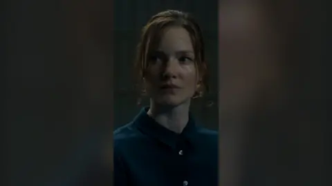 Character Rachel wears a blue shirt and looks to her right.