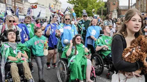 Stockton Borough Council People, some in wheelchairs, dressed in colourful clothing and carrying flags.