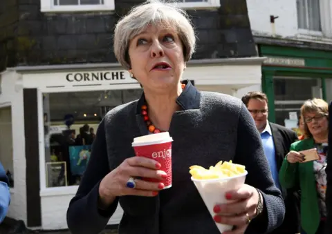 Getty Images Theresa May holding a hot drink and some chips