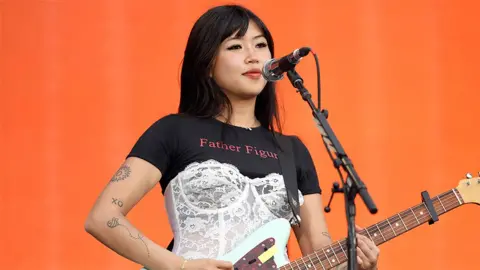 Getty Images Beabadoobee playing a guitar at a concert with an orange background