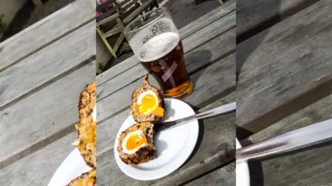 Image of a Scotch egg cut in half, next to a pint.