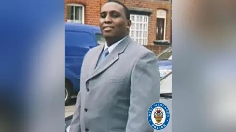 West Midlands Police A man with short-cropped black hair is wearing a light grey suit jacket over a white shirt and pale blue tie. A West Midlands Police logo has been superimposed in the corner of the picture.