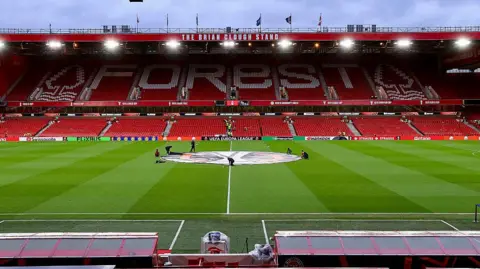 A low shot of the Nottingham Forest home pitch, with a tall, red and white football stand in the background 