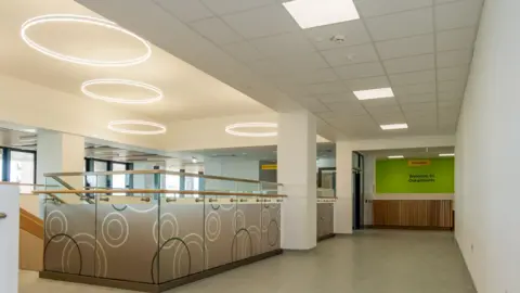 Supplied The main staircase of the new eye hospital leading to the out-patients gree reception area. Glass panels surround the stairs with circular lamps on the ceiling.