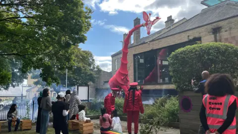 BBC People looking up at a giraffe puppet at a library in Bradford