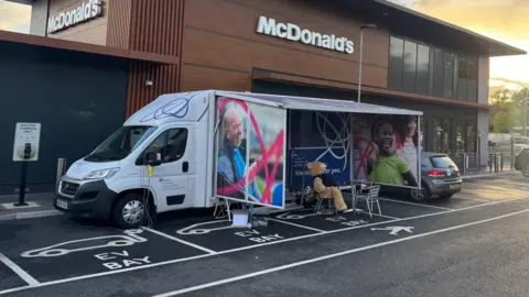SUPPLIED A white van with a fold out awning is parked in a car park outside a Mcdonald's drive through.