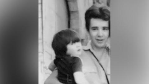 A black and white picture from the 1970s of a young man holding a little boy