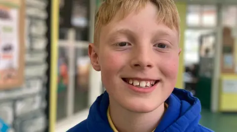 a close up of a blond-haired boy smiling at the camera
