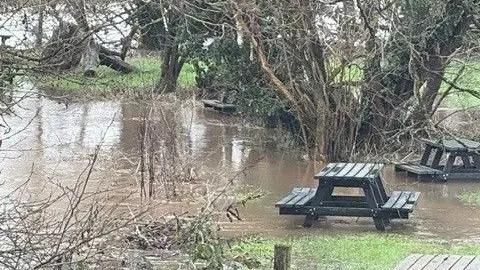 Nicky Woodrow A picture of two picnic benches submerged in flood water surrounded by trees