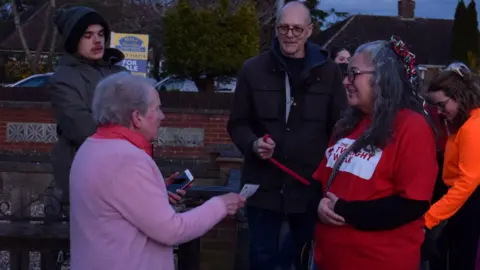Barney Devereux A woman donating money to a group of people in Rushden