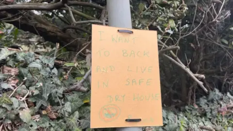 BBC Child's handwritten poster saying "I want to back and live in safe dry house"