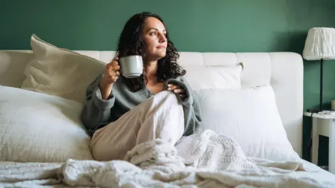 A woman in bed drinking a cup of tea