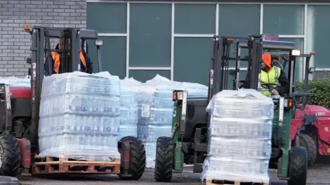 PA Media Two forklifts driving outdoors, carrying pallets of bottled water.