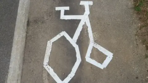 A strange-looking line-drawing of a bicycle painted in white paint on a road