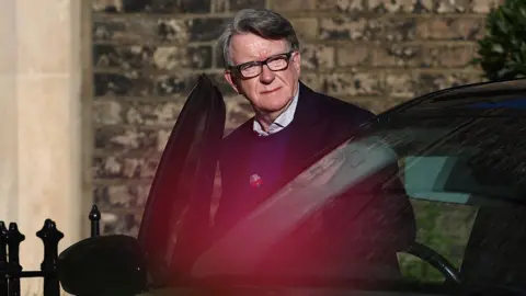 AFP Lord Peter Mandelson stepping into a black-tinted car, wearing thick black frames.