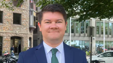 Deputy Sam Mézec is wearing a blue suit and a green tie
