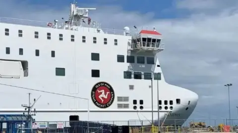 BBC The bow of the Manxman, which is a tall white angular ferry, with the Isle of Man Steam Packet's logo on the side, which is the three legs of Man with the words Isle of Man Steam Packet Company around it.