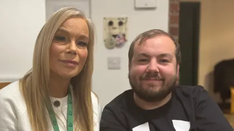 Trish Marr and her son David. Ms Marr has long blonde hair and is wearing a white jumper. David has short brown hair and a beard. 