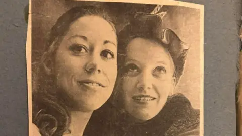 Judy Shone A black and white photo, mounted on grey paper, of two women with dark hair.